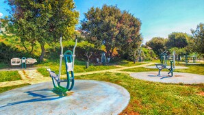 A park with exercise equipment, benches, and trees.