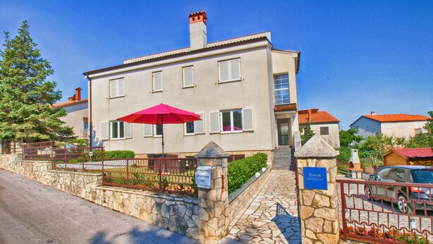 A two-story building with a stone facade, a red umbrella, and a sign indicating it is an apartment.