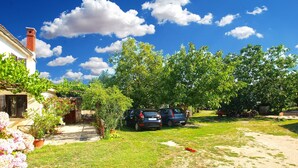 Zona residencial con una casa, coches aparcados y un jardín.