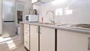 Una cocina moderna con armarios blancos, un refrigerador de acero inoxidable, un microondas, una cafetera y un lavamanos con grifo.