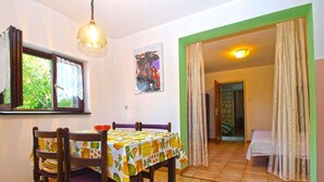 A dining area with a table set for four, wooden chairs, a patterned tablecloth, a window with curtains, a painting on the wall, and a doorway leading to another room. - Apartment 1453/13446 (Istria - Banjole), 100m from the beach (Banjole)