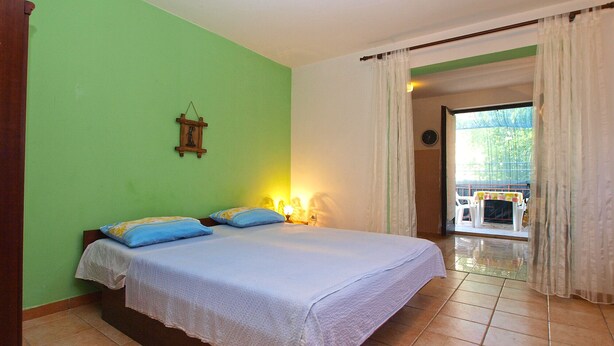 A bedroom with a bed, pillows, a nightstand, a wall clock, and a view of the outside. - Apartment 1453/13446 (Istria - Banjole), 100m from the beach (Banjole)