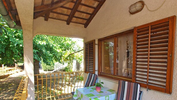 A covered outdoor seating area with a table and chairs, a railing, and a view of greenery. - Apartment 1457/13488 (Istria - Rovinj), 1000m from the beach (Rovinj)