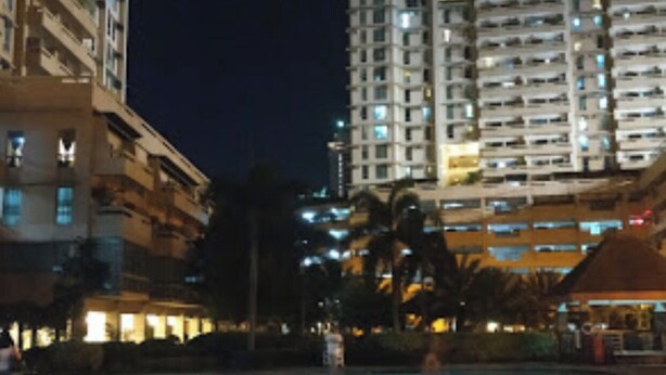 Vista nocturna de una zona de piscina con rascacielos al fondo.