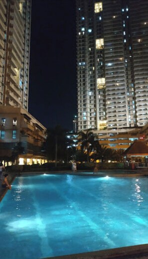A nighttime view of a swimming pool area with high-rise buildings in the background. - 2 bedroom condo available at Tivoli Garden Residences Luxury Resort makati  (Metro Manila)