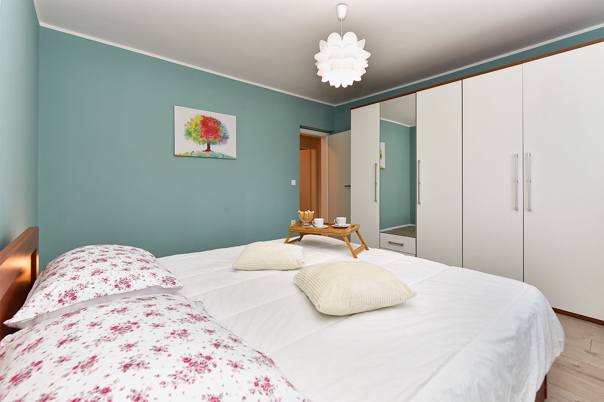 A bedroom with a bed, a bedside table, a chair, a wardrobe, and a painting on the wall.