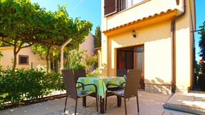 An outdoor patio with a table and chairs, surrounded by greenery and a building with a tiled roof. - Apartment 1482/13875 (Istria - Medulin), 600m from the beach (Medulin)