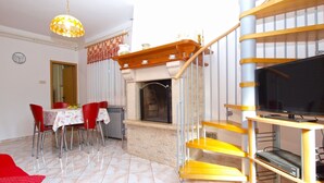 A modern living room with a fireplace, a dining area with red chairs, a TV on a wooden stand, and a staircase with a yellow railing. - Apartment 1482/13875 (Istria - Medulin), 600m from the beach (Medulin)