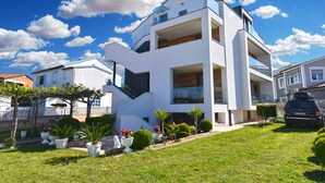 A modern two-story house with a white exterior, large windows, and a well-maintained garden with potted plants and a lawn. - Apartment 1490/14261 (Istria - Fažana), 350m from the beach (Fažana)