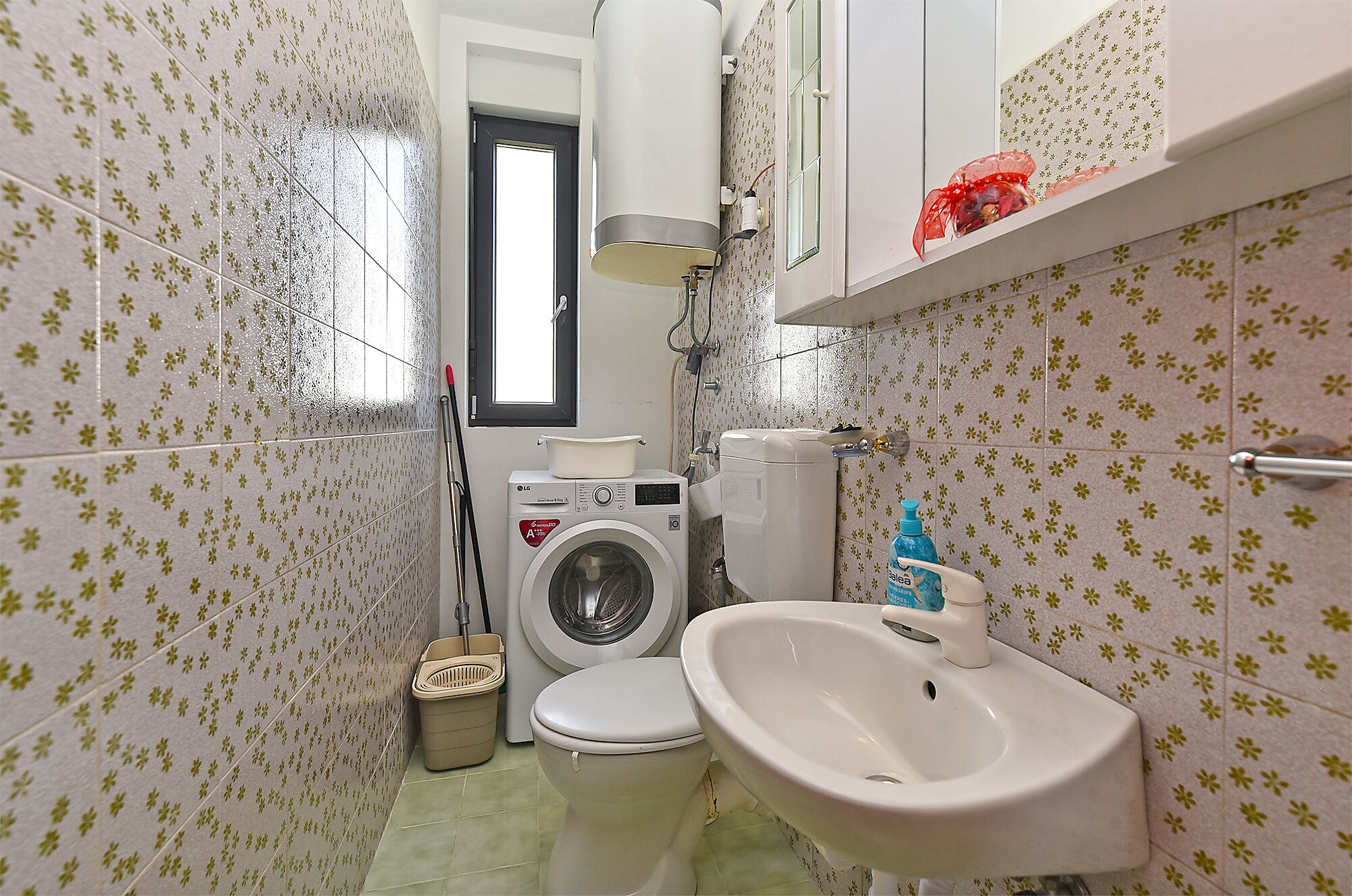 A compact bathroom with a washing machine, toilet, and sink.