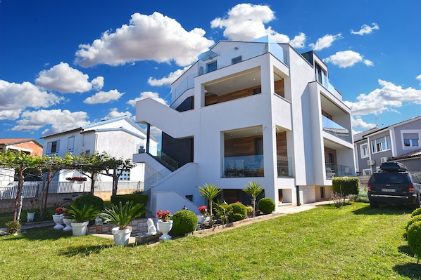 A modern two-story house with a white exterior, large windows, and a well-maintained garden with potted plants and a lawn.