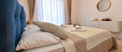 A neatly made bed with a quilted cover, a bedside table with a mirror, and a small shelf with decorative items.