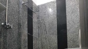Un baño con piso de mármol, inodoro blanco y zona de ducha con un estante metálico.
