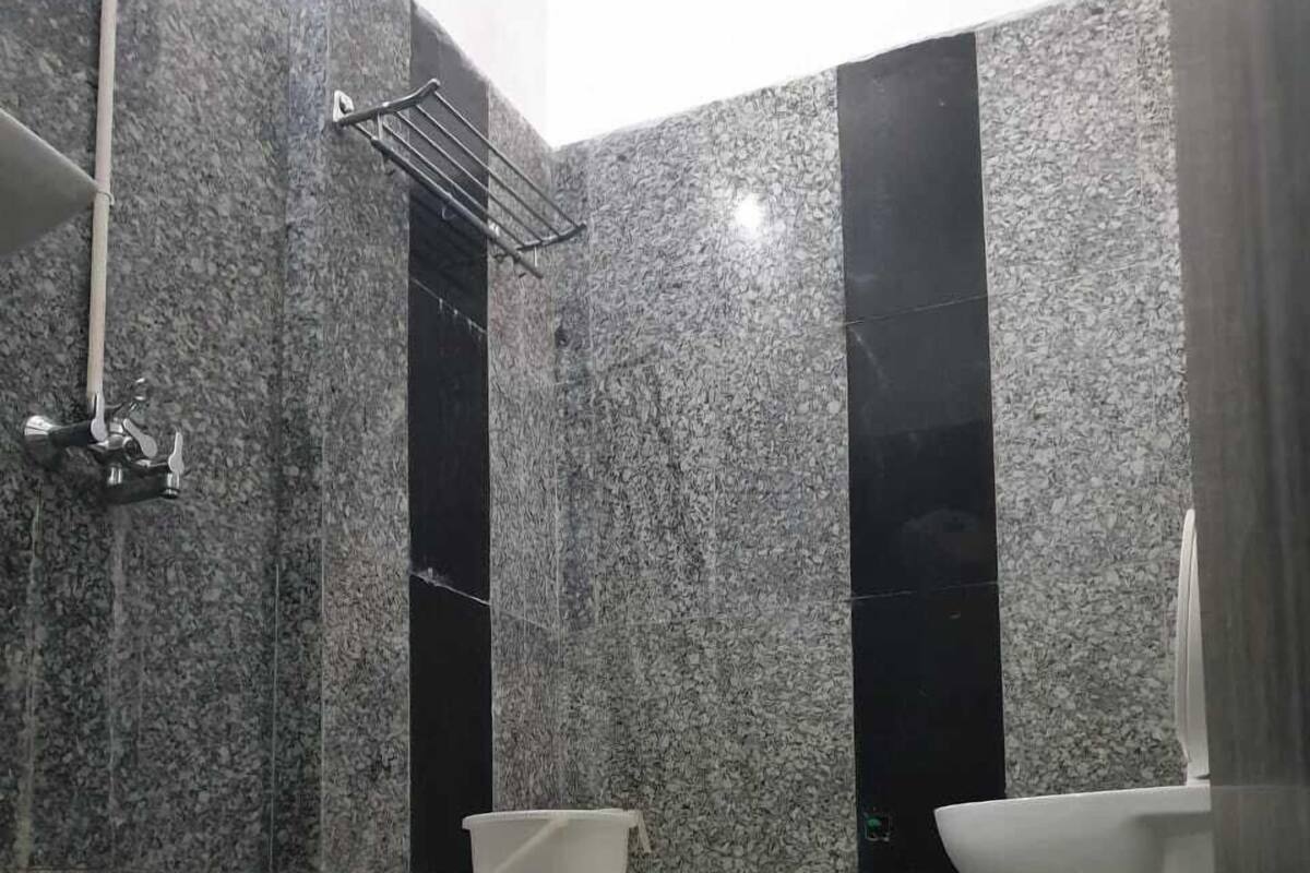 Un baño con piso de mármol, inodoro blanco y zona de ducha con un estante metálico.