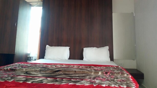 Un dormitorio con cabecera de madera, cama con ropa blanca y manta estampada en rojo y gris.