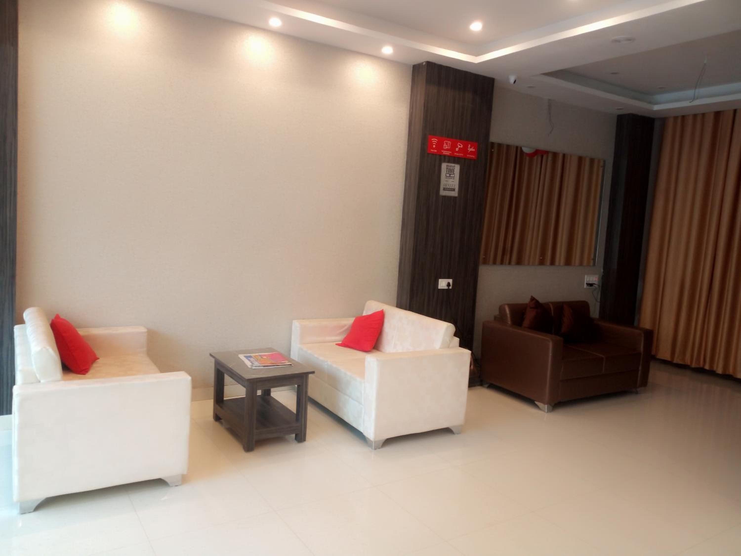 A modern hotel lobby with white sofas, a small table, and a dark column with a red sign.