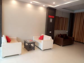 Un lobby moderno de hotel con sofás blancos, una mesita y un pilar oscuro con un letrero rojo.