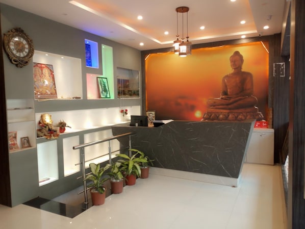 A reception area with a marble counter, potted plants, and a Buddha statue in the background.
