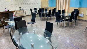 Un salón de conferencias con mesas redondas de vidrio y sillas negras, un mostrador de recepción y una pared cubierta de papel tapiz floral.
