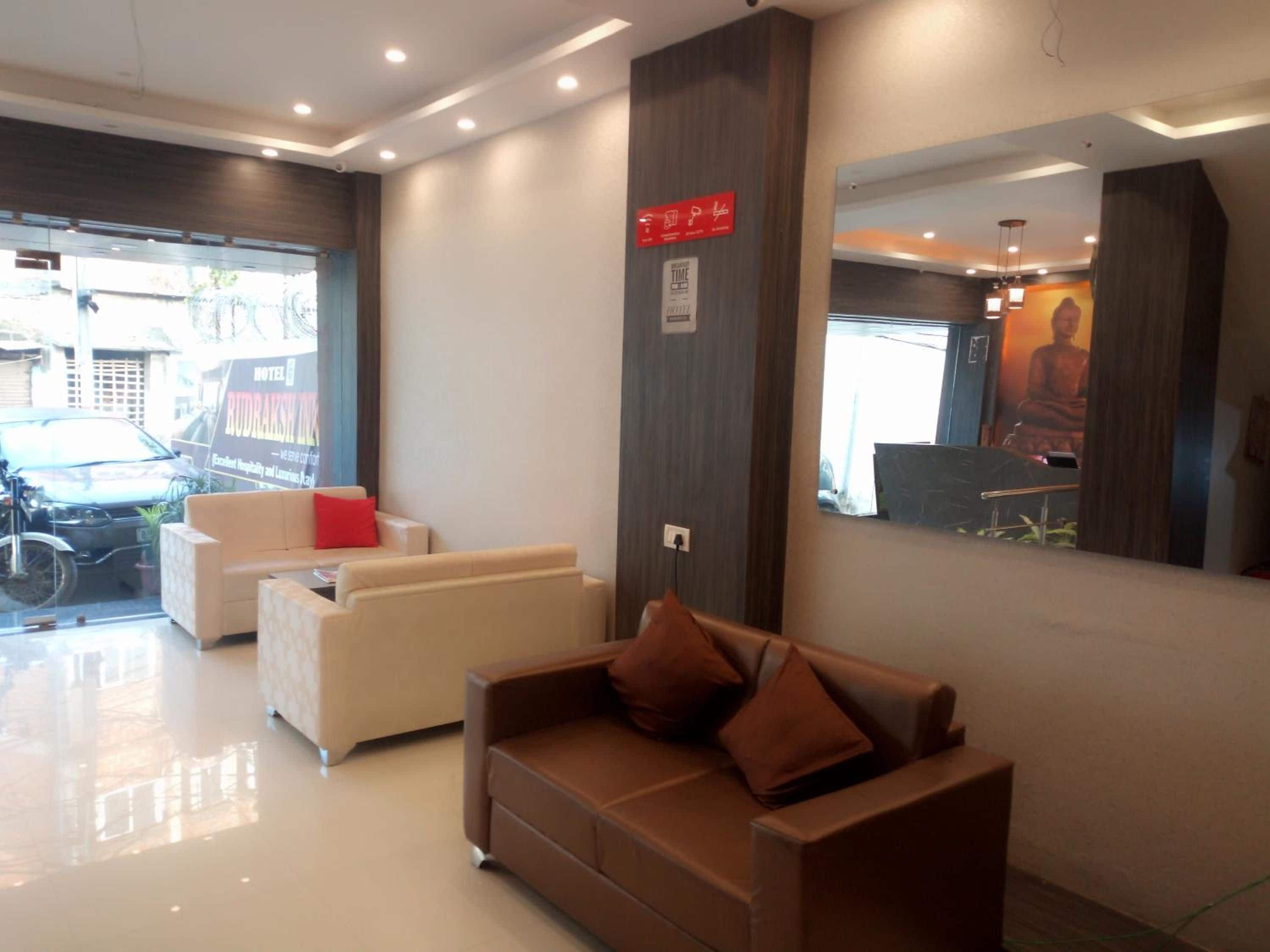 Zona de recepción de un hotel con diseño moderno, que incluye un mostrador de recepción, un área de descanso con sofás y un espejo grande que refleja el interior.