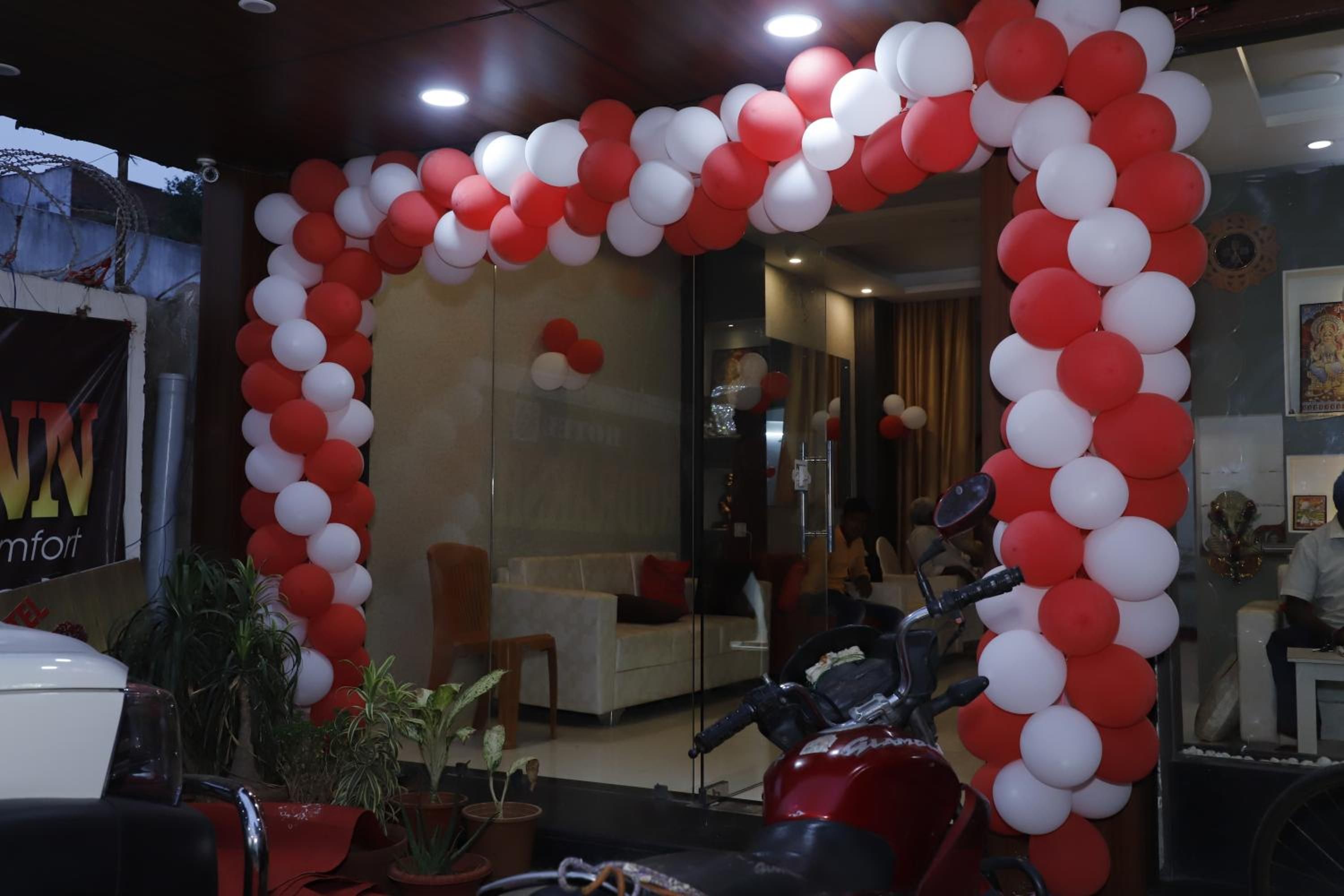 A reception area with a red and white balloon arch, a white car, and potted plants.