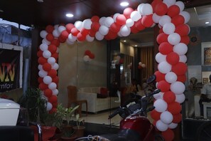 Un área de recepción con un arco de globos rojo y blanco, un coche blanco y plantas en macetas.