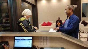 A reception desk with a laptop, a telephone, and a sign indicating 'Excellent Host.' - Hotel Rudraksh Inn (Narendranagar)