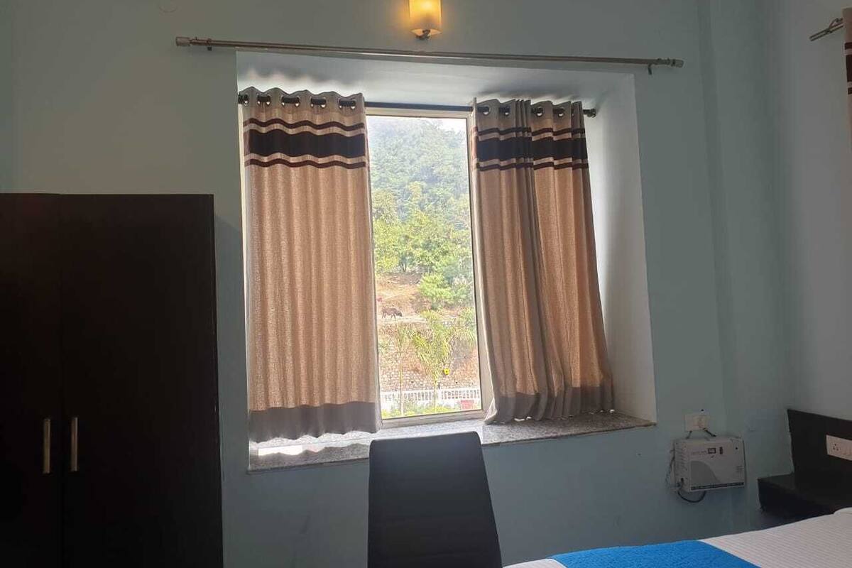 Una habitación con cama, ventana con cortinas, calentador en la pared y vista a zonas verdes.