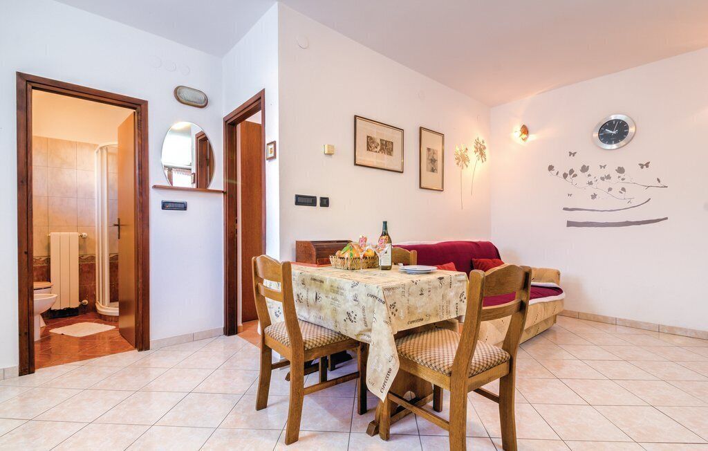 Un área de comedor con una mesa lista para dos personas, sillas de madera, un sofá rojo y una pared decorada con cuadros y un reloj.