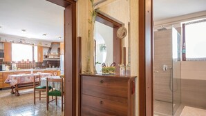 A modern kitchen with wooden cabinets, a dining table, and a view into the adjacent bathroom.