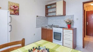 Cocina compacta con estufa, horno y alacenas de madera. Cuenta con una mesa de comedor con sillas y un cuadro en la pared.