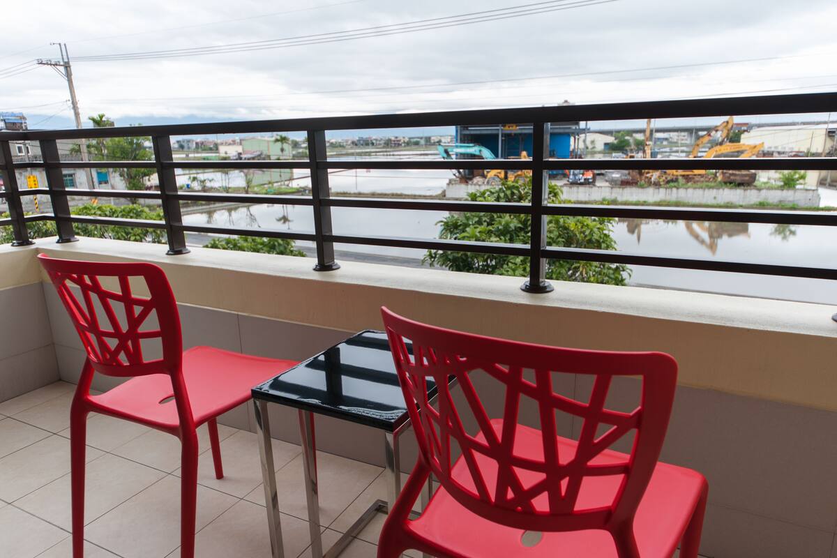 A balcony with two red chairs and a small table, overlooking a construction site with heavy machinery.