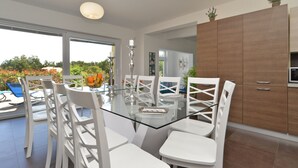 A modern dining area with a glass table and white chairs, a wooden cabinet, and a view of the outdoors. - Villa 1519/15239 (Istria - Žminj), 25000m from the beach (Žminj)