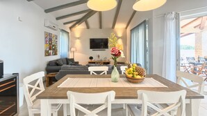 A dining area with a wooden table, white chairs, and a vase with flowers. There is a television in the background and a window with curtains. - Villa 1521/15241 (Istria - Žminj), 25000m from the beach (Žminj)