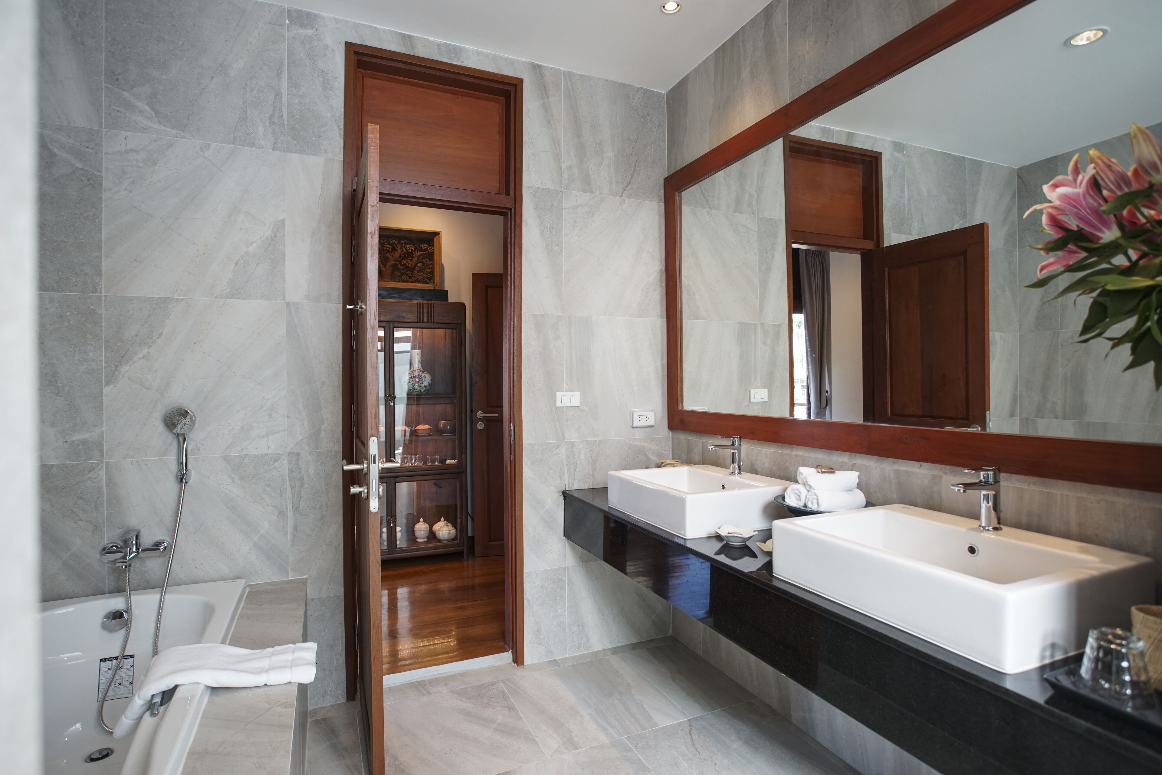 Un baño moderno con un espejo grande, dos lavamanos, una ducha y un armario de madera.