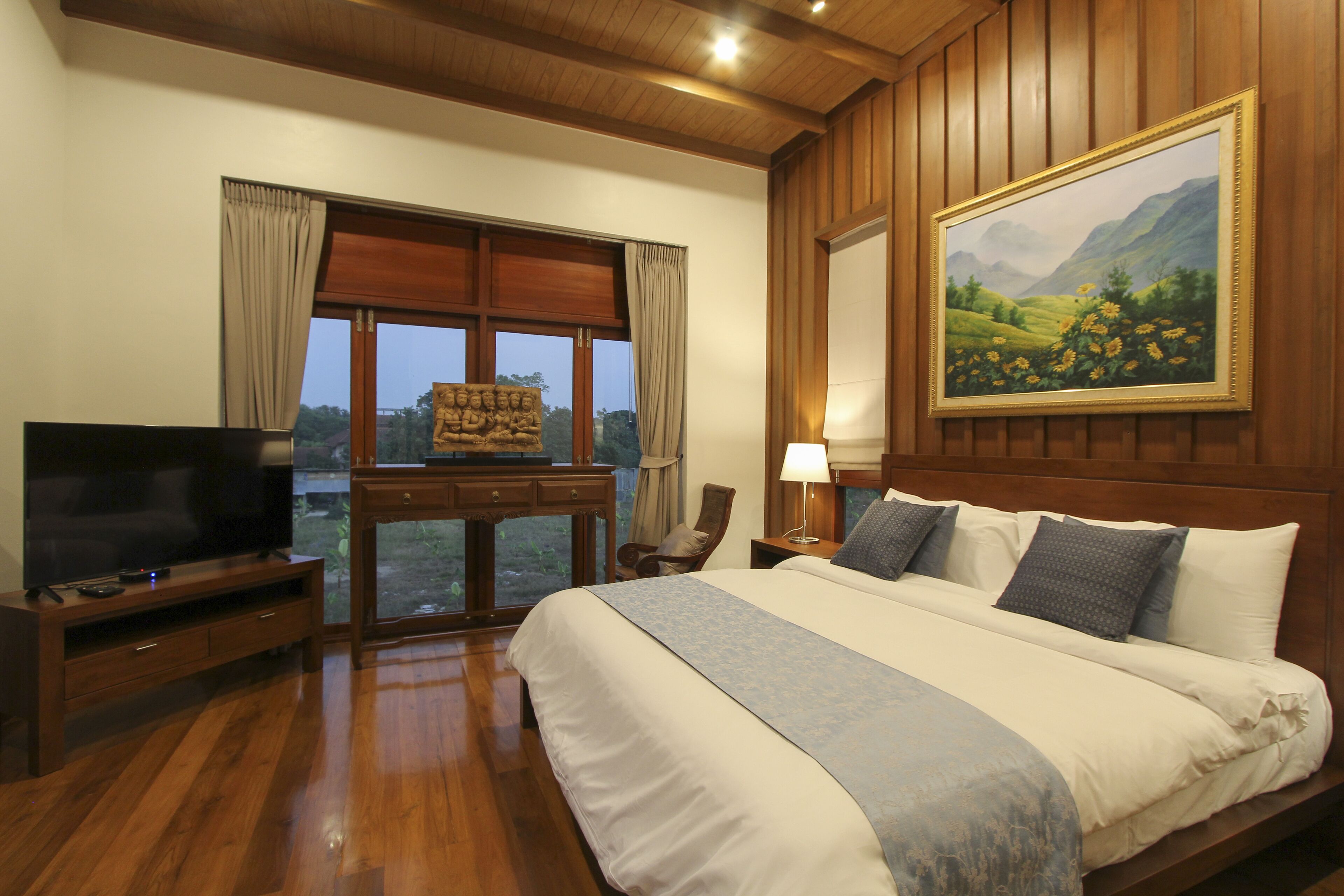 Une chambre d’hôtel avec un grand lit, des meubles en bois, un tableau au mur et une vue sur l’extérieur par une fenêtre.