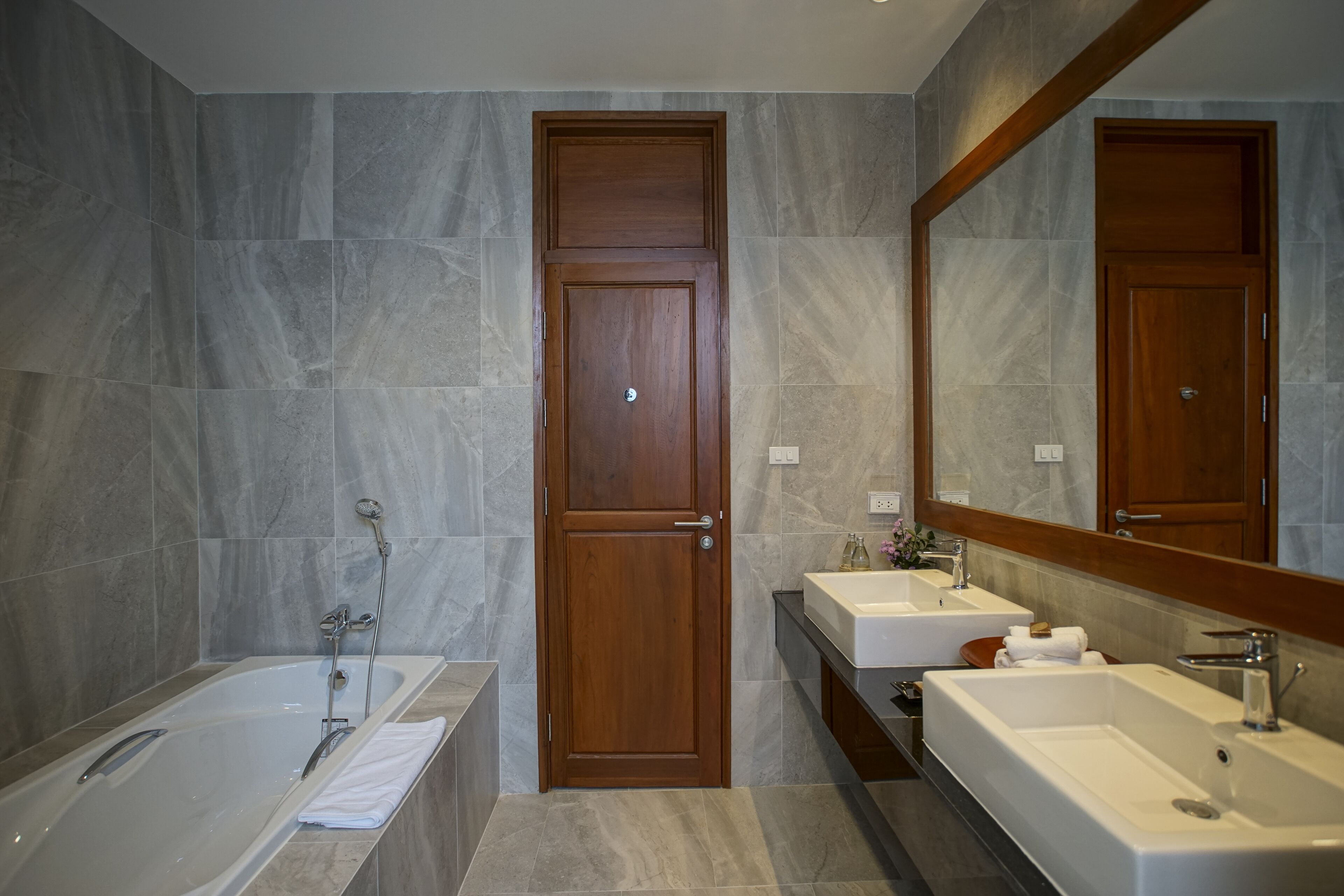 Un baño moderno con lavamanos doble, bañera y puerta de madera.