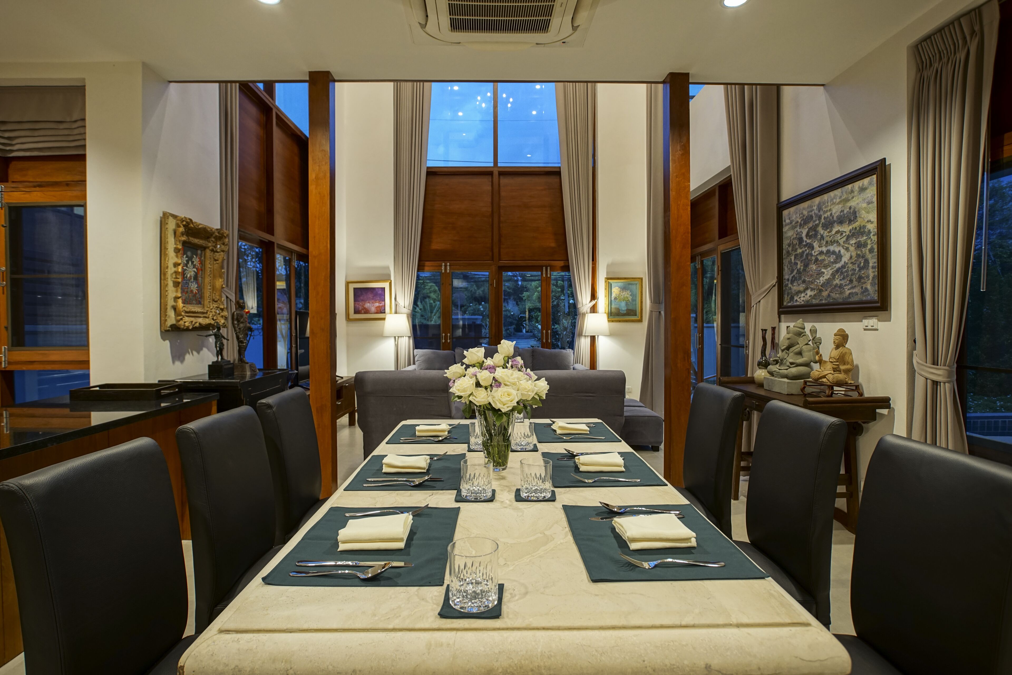 A dining area with a long table set for a meal, flanked by chairs, with a vase of flowers in the center.