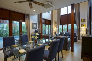 Uma área de jantar moderna com mesa de vidro, cadeiras azuis e vista para o exterior.