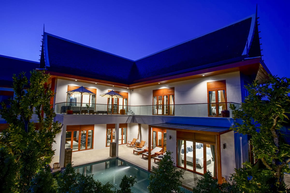 Una casa de varios pisos con piscina, mobiliario exterior y un patio cubierto.