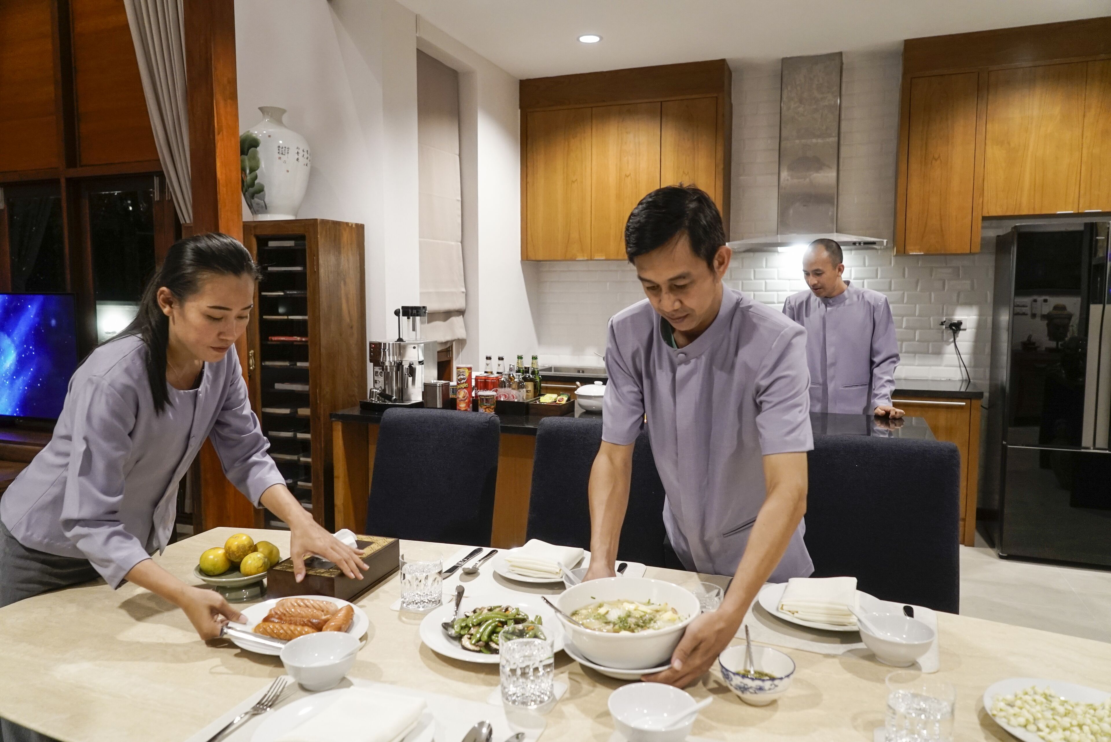 A modern kitchen with wooden cabinets, a dining table set for four, and various kitchen appliances.