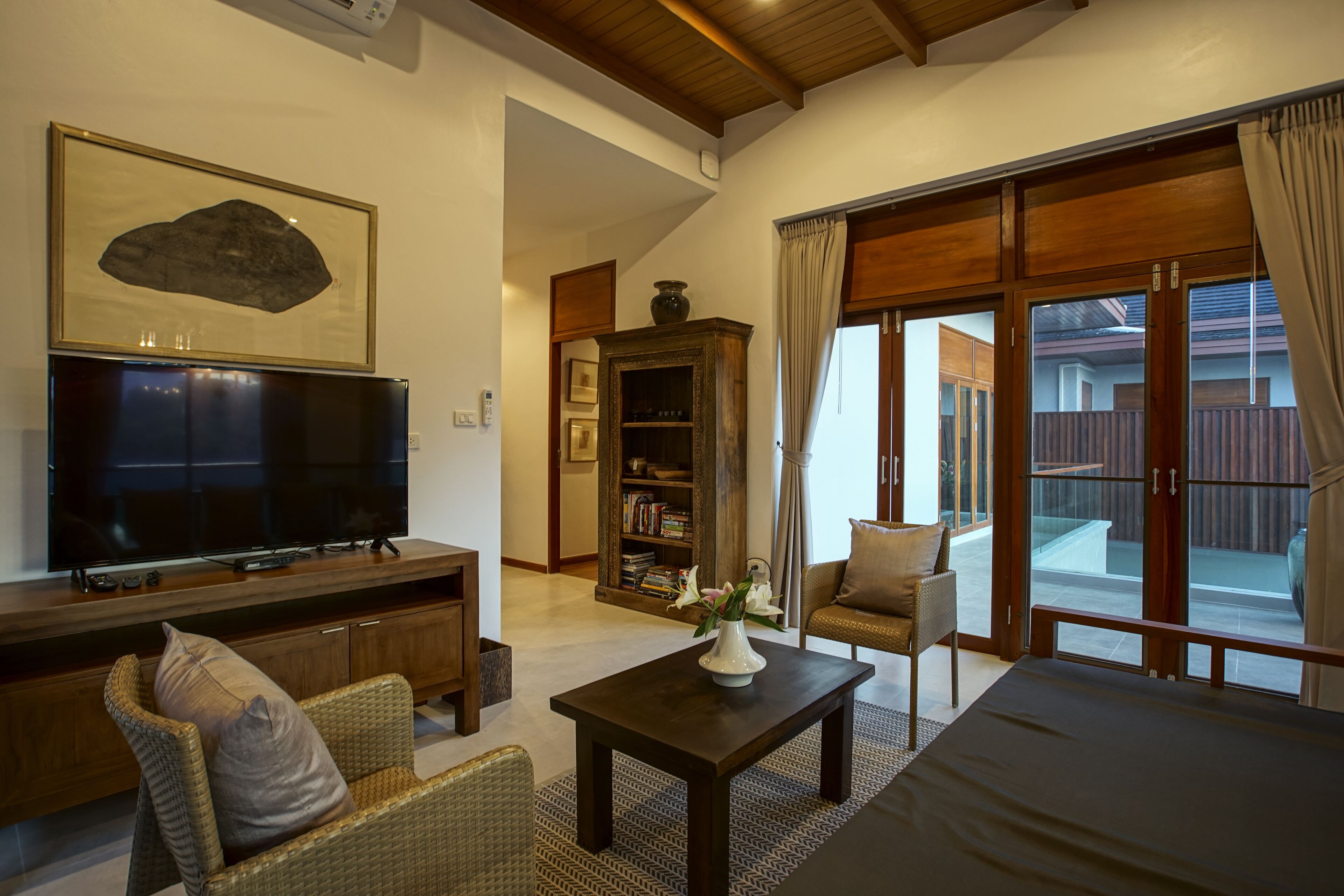 A living room with a flat-screen TV, wicker furniture, a bookshelf, and a large sliding glass door leading to an outdoor area.