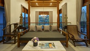 Una habitación con cama, sillas de madera, una mesa de centro con revistas y un jarrón de flores.