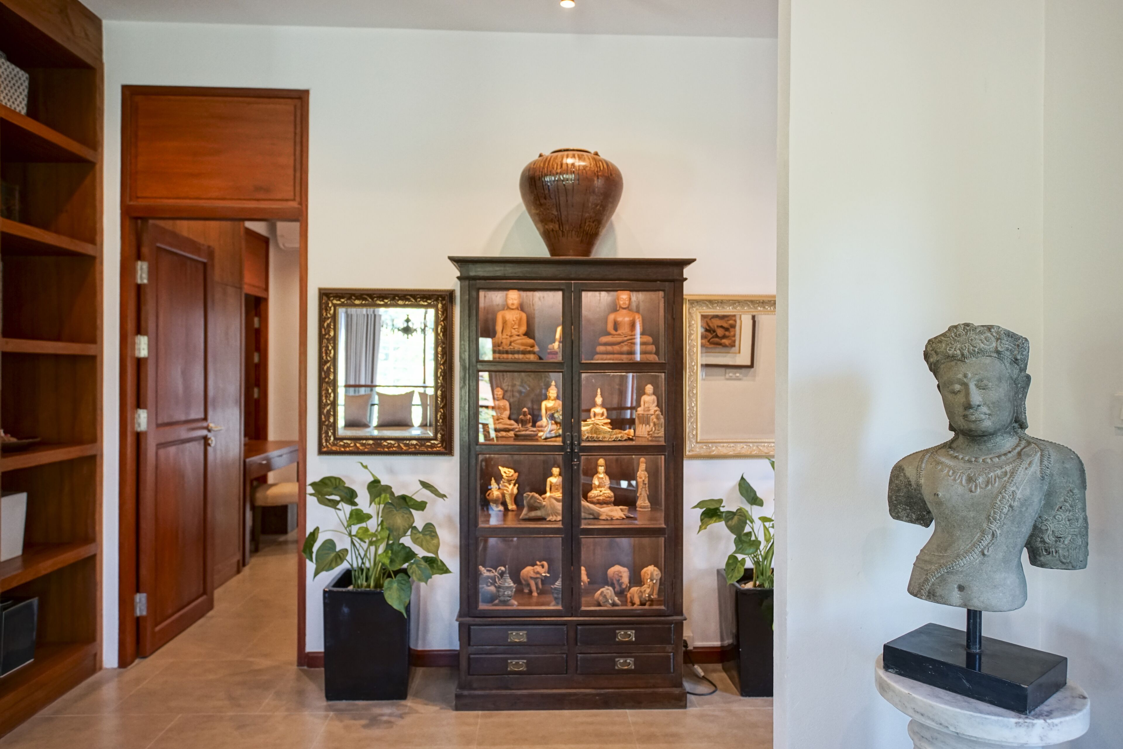 Un pasillo con un aparador de madera que exhibe estatuas de Buda, un busto y cuadros enmarcados en la pared.