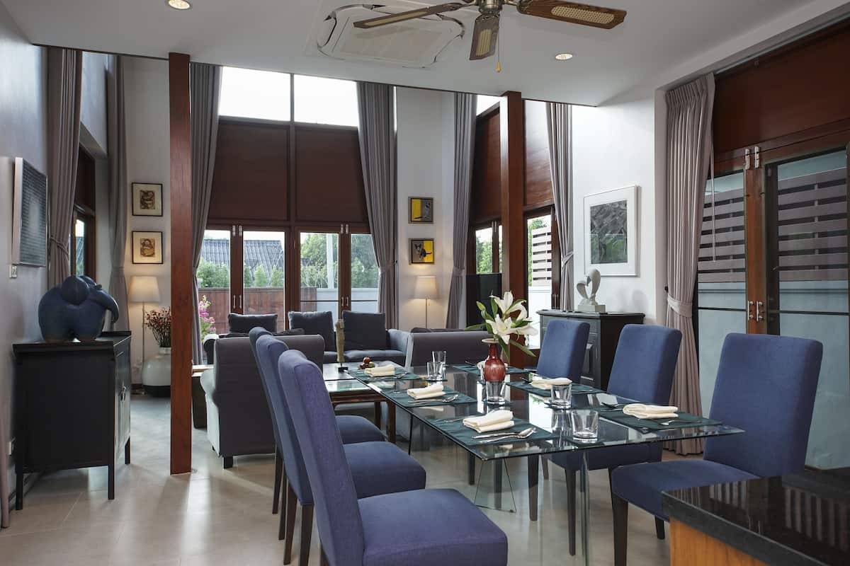 Un comedor moderno con una mesa de vidrio, sillas tapizadas en azul y vistas al exterior a través de amplias ventanas.