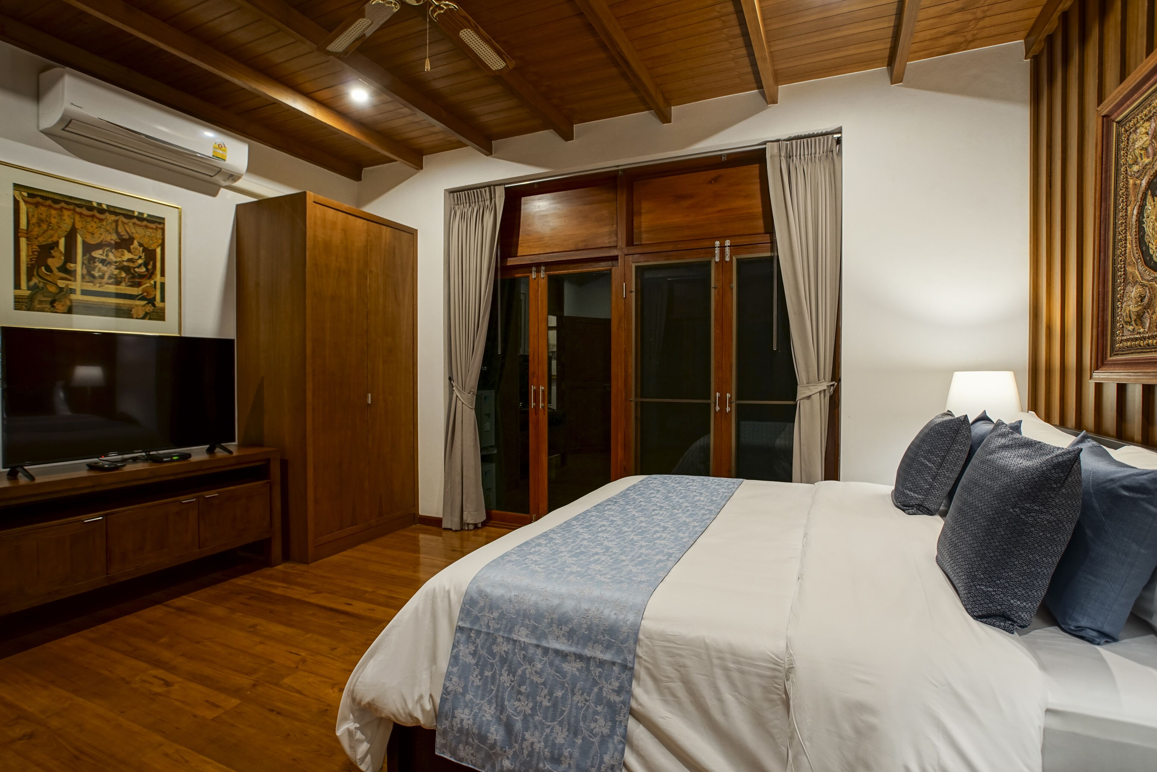 Une chambre avec un grand lit, une télévision, des meubles en bois et une porte-fenêtre coulissante.