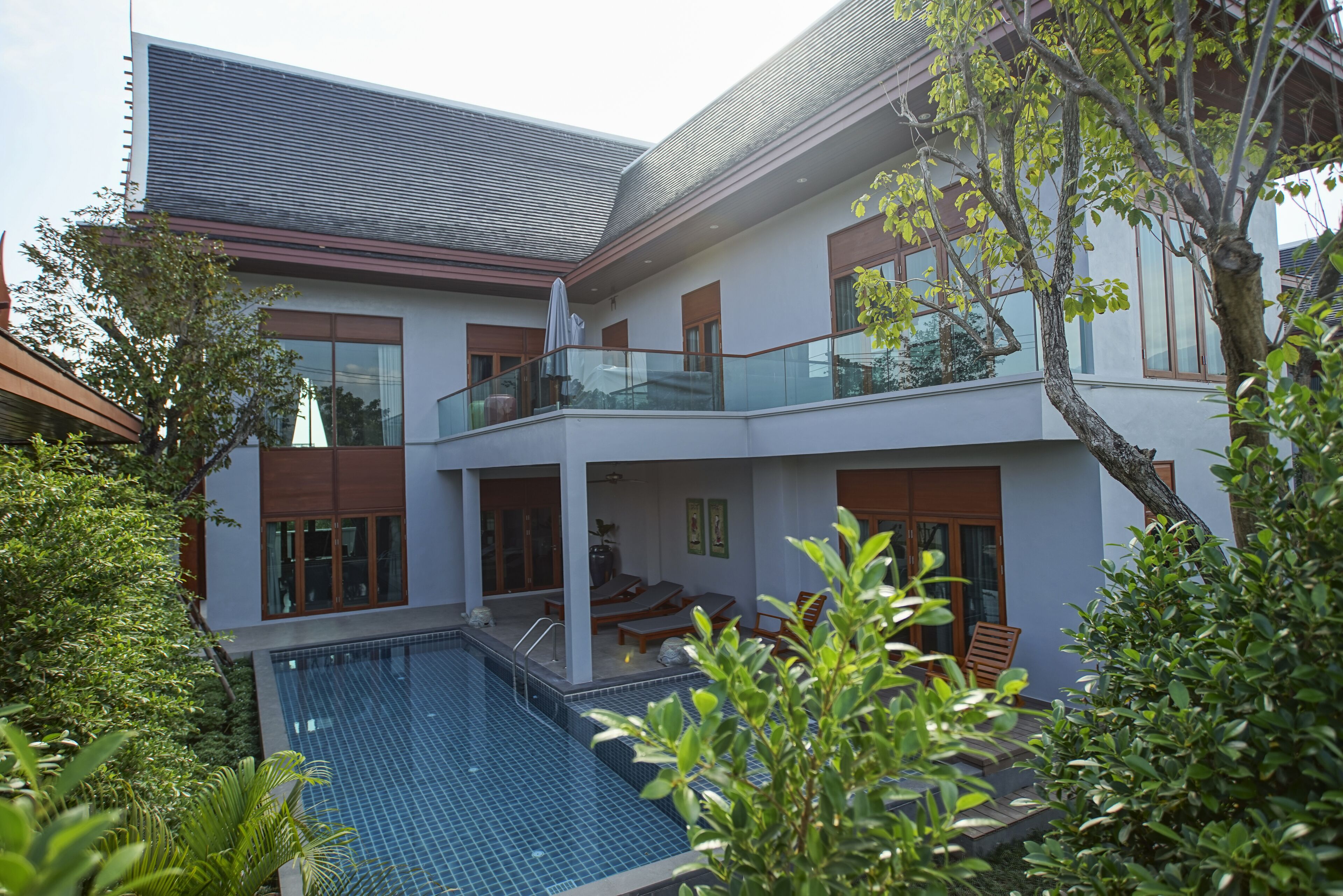 A modern two-story house with a swimming pool, large windows, and a balcony.