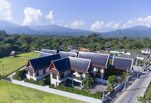 Área residencial com casas modernas, coberturas inclinadas e janelas amplas, cercada por vegetação exuberante e montanhas ao fundo.