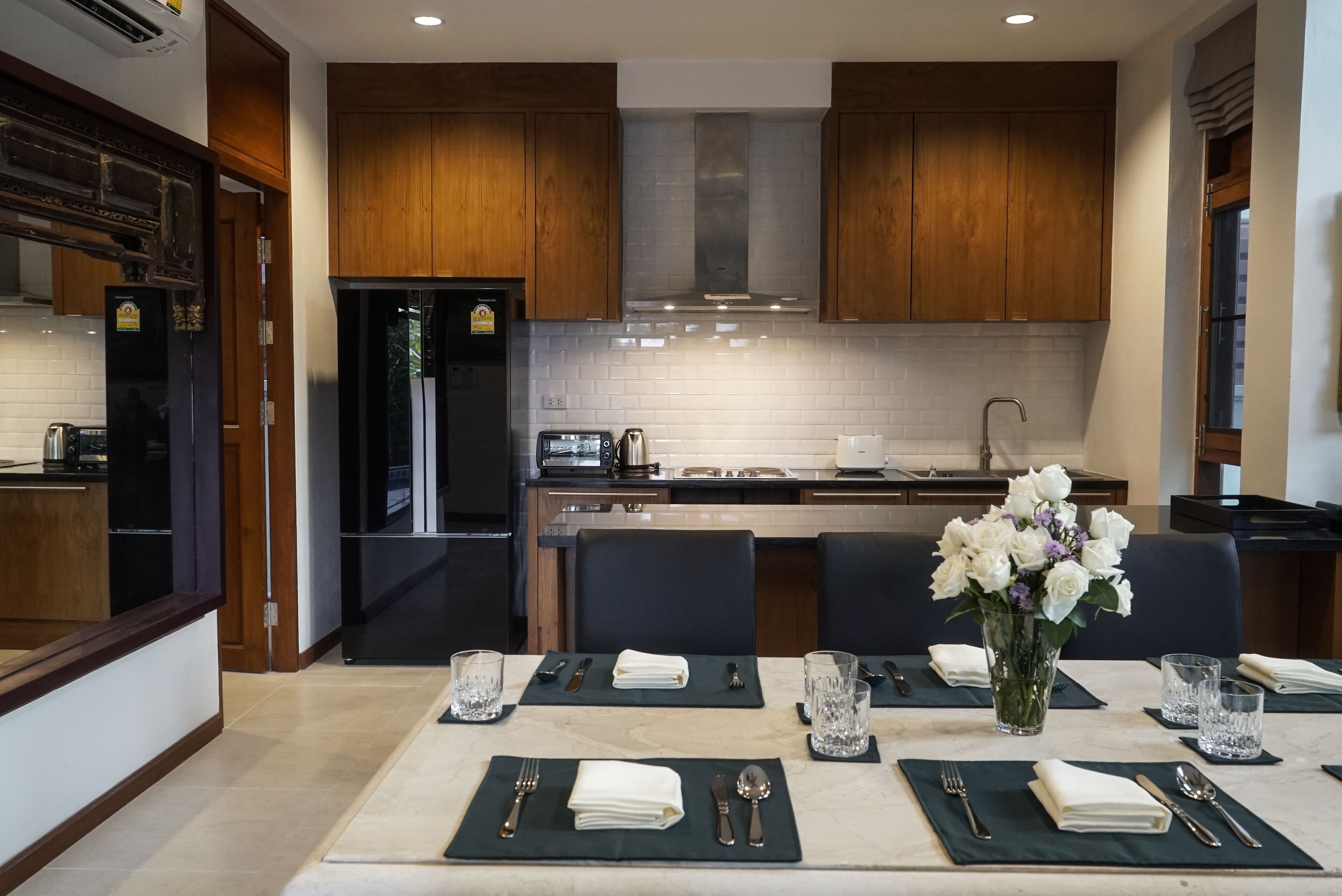 Eine moderne Küche mit Holzausstattung, einem Edelstahlkühlschrank und einer Essecke mit Tisch, Stühlen und einem Blumenstrauß.