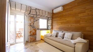 A living room with a stone wall, wooden paneling, a sofa with cushions, a small table with a lamp, and a sliding glass door leading to an outdoor area. - Apartment 1531/15377 (Istria - Vinkuran), 500m from the beach (Vinkuran)